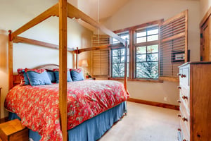 Dreamy guest bedroom with wooden canopy king bed and two large picture windows with wooden shades