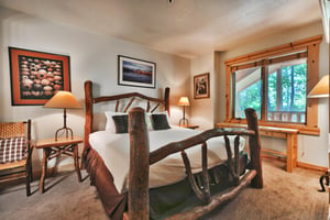 First bedroom with log bedframe and luxurious king bed, large picture window overlooking the mountainside