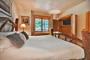 King bed with white linens, wooden bedframe, large wooden armoire with flat screen TV
