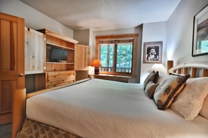 King bed with white duvet, large wooden armoire with flat screen TV