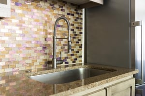 Iridescent tiled backsplash behind the chrome kitchen sink, granite countertops