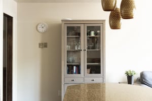 Grey wooden hutch in the kitchen area with glass cabinets and artful pendant drop lights in the foreground