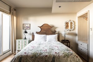 Comfortable queen bed in the bedroom with striking decorative wooden headboard with bird, window wall for abundant natural light and build in wall closet and dresser set