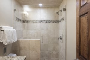 Spacious shower with chrome finishes, tiled shower walls with glass panel door