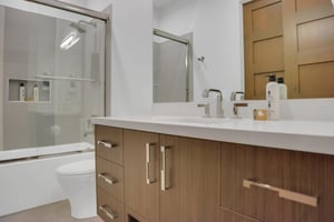 Vacation rental bathroom with light grained wood and gold hardware, and a bathtubshower combination.