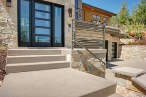 Vacation rental entry with large glass windows and doors and stone façade.