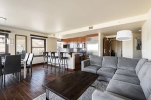 Large gray sectional in the living room wraps around a modern wood top coffee table with the kitchen in the background