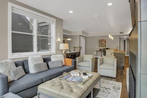 Rio Grande 202s living room with large window, a grey couch, light colored club chairs, and leather covered coffee table.