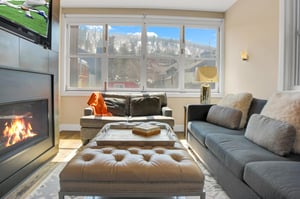 iving room with a grey upholstered couch and loveseat, leather ottoman, and large picture window with mountain view.