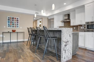 Waterfall granite island with four black bar height stools and pendant lighting above the island.