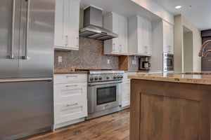 A beautiful kitchen with white cabinets, granite backsplash, stainless steel appliances, and wood floors.