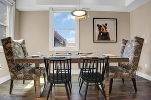 Comfortable upholstered chairs at the head of a wooden table and four black wooden chairs.