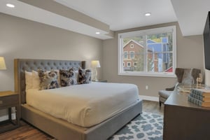 A grey upholstered kingsize bed with stylish furnishings and serenecolored walls, overlooking town and mountain views.