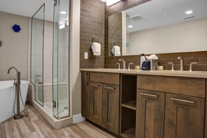 Beautiful wood vanity with double sinks and lightcolored tile walkin shower with glass surround.