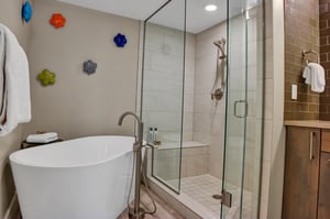 Standalone soaker tub and walkin shower with colorful ceramic flower art on the wall.