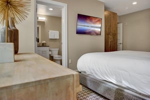 The bedroom with a wall mounted TV, wooden armoire and dresser, and attached bathroom.