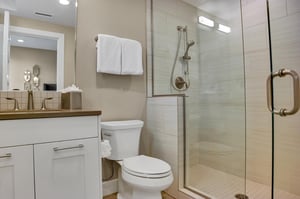 The ensuite bathroom with cream colored tiled shower with glass surround, white vanity with grey counter and toilet.