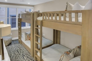 Two light colored wood bunkbeds, pushed end to end with orange and grey zig zag throw pillows and large window.