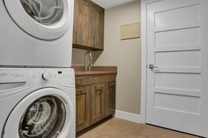 Stacked washer and dryer with wooden cabinet storage and sink.