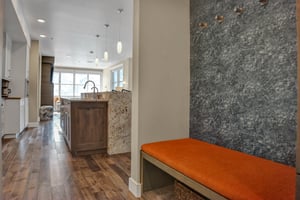 Entry bench with orange cushion and grey wall with hooks to hang jackets from.