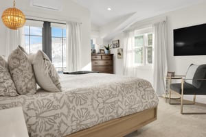 The main suite has crisp white walls and drapes, a dark wood dresser, and double doors leading to a patio.