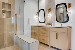 Main bathroom with dual sink wood vanity and quartz slab counter and accent wall, with a glassenclosed shower.