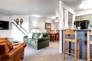 Snow Flower 12s open concept living room, dining area and kitchen with breakfast bar, crisp white walls and wood accents.
