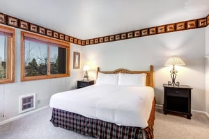 Snow Flowers main suite has a king size bed with white linens, 2 end tables and lamps and wall paper border around the walls.