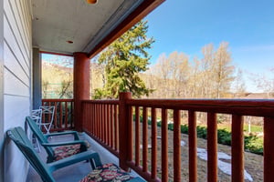 Snow Flower 12s deck with wooden railing, chairs, overlooking many trees and blue sky.