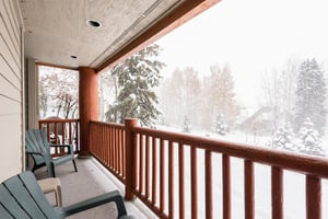 Snow Flower 12s deck with wooden railing, chairs, overlooking many trees and a snowy wintery day.
