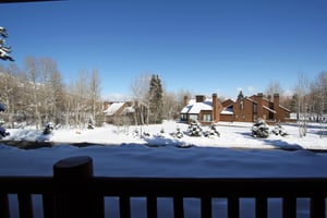 Snow Flower 12s deck with wooden railing and an open field of snow with houses beyond and blue sky.