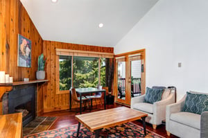 Snow Flower 29s living area with 2 cream colored upholstered chairs, wood coffee table, fireplace and glass doors to patio.