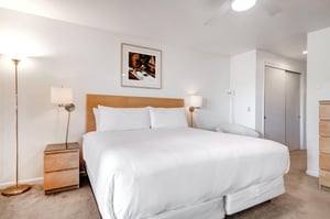 Snow Flower 29s main suite king size bed with wooden headboard, crisp white linens, 2 end tables and lights, and white wall.