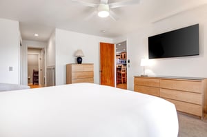 Snow Flower 29s main suite king size bed with crisp white linens, 2 wooden dressers, flat screen TV and white walls.