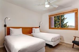 Bedroom 3 has 2 twin beds with crisp white linens, wood headboard with 2 attached lights, shared night stand and a window.