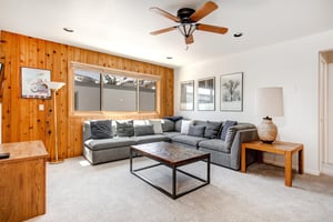 Loft living area with a large grey sectional couch and wood paneling on one wall and white paint with pictures on the other.