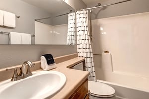 A bathroom with wooden cabinets, cream colored counter, single sink, white toilet and bathtubshower combination.