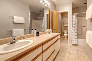 Two sink vanity with wood and white cabinets, cream counter, large mirror and vanity light, and separate water closet.