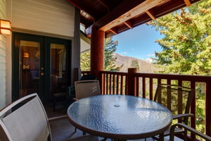 Snow Flower 29s deck with wooden railing, round table with 4 chairs, and evergreen trees and blue sky beyond.