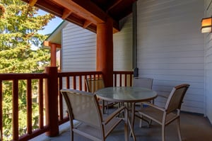 Snow Flower 29s deck with wooden railing, round table with 4 chairs, and evergreen trees and blue sky beyond.