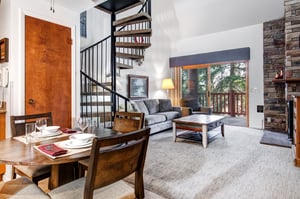 Open concept dining room and living room with a spiral staircase made of iron and wood, white walls and sliding glass doors.