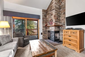 Snow Flower 31s living room with floor to ceiling stone hearth, gas burning fireplace, grey seating, and wood coffee table.