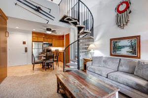 Snow Flower 31s living room with grey upholstered couch, spiral staircase and mixed color wood coffee table.