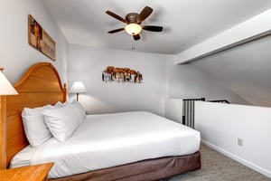 Snow Flower 31s loft with a king size bed with crisp white linens, night stands with lamps, stair entry, and picture on wall.