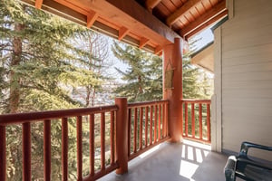 Snow Flower 31s deck with wooden railing and evergreen trees and blue sky beyond.