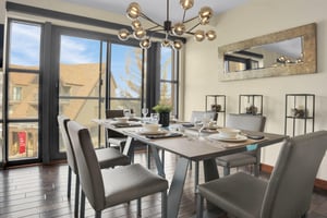 A modern dining table with 6 chairs and place settings, large windows and sliding doors leading to a patio, and chandelier.