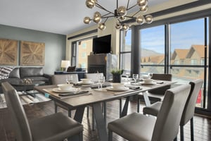 A modern dining table with 6 chairs and place settings, large windows and sliding doors leading to a patio, and chandelier.
