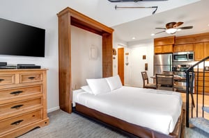 Snow Flower 31s living room with a Murphy Bed made with white linens, wood dresser, and wall mounted TV above it.