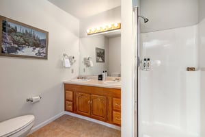 Bathroom with wood cabinet, two sink vanity, walkin shower with glass enclosure, tan tile floor and griege walls.