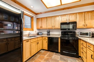 Snow Flower 43s kitchen with black appliances, oak cabinets, large overhead lighting, and tile floor.